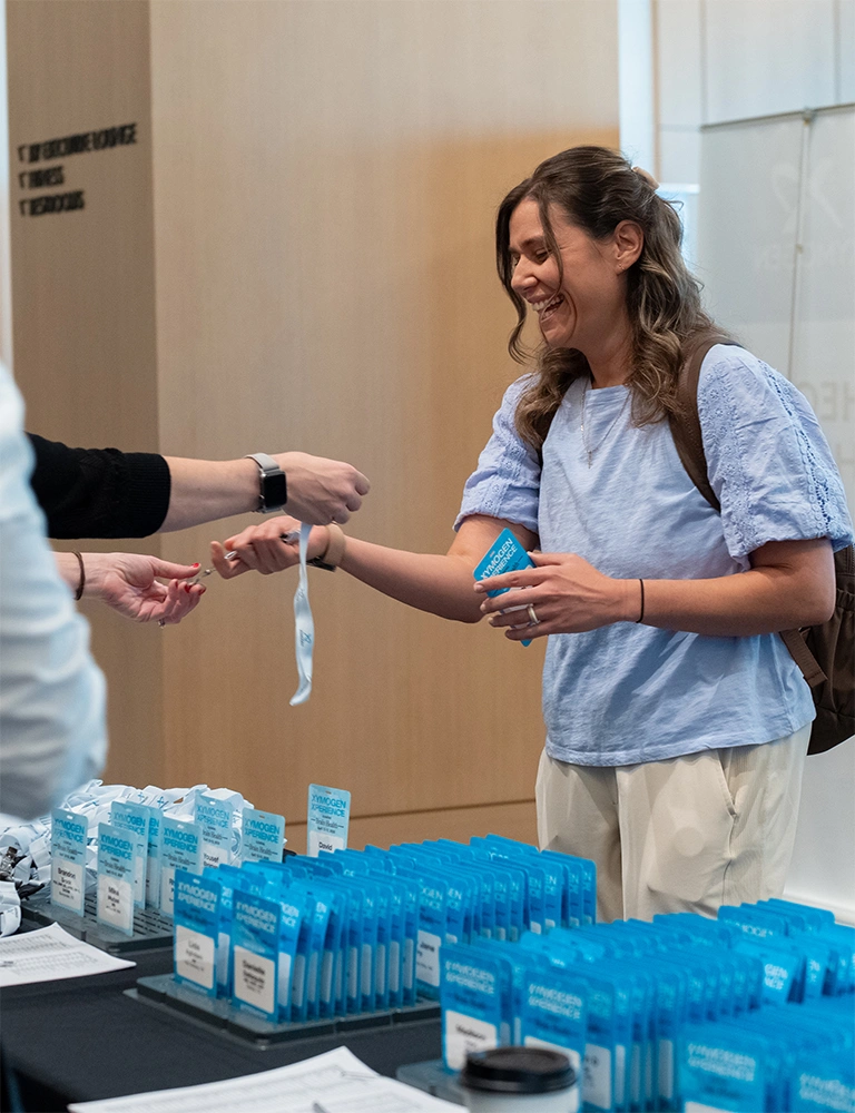 A smiling conference attendee receiving their wristband and ID card